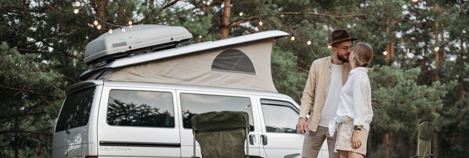 A couple shares a romantic moment by their camper van in a serene outdoor setting.